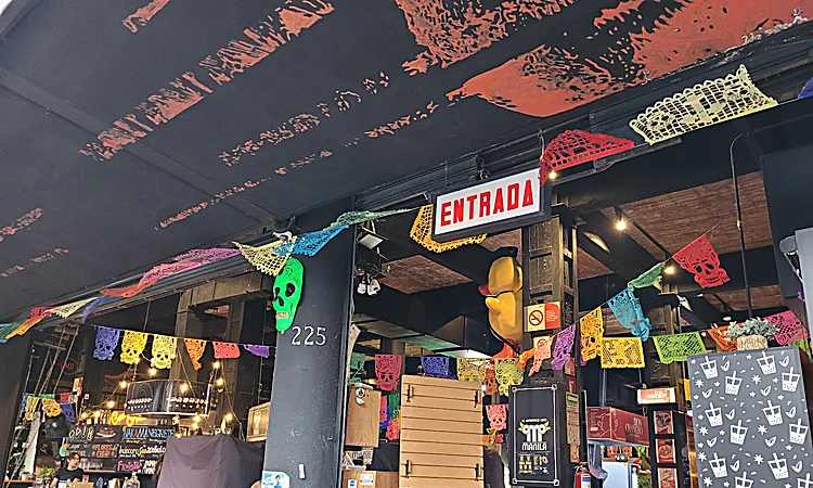 Interior de Mercado Roma con papel picado de colores, el letrero rojo de ENTRADA y el número 225 en una columna.