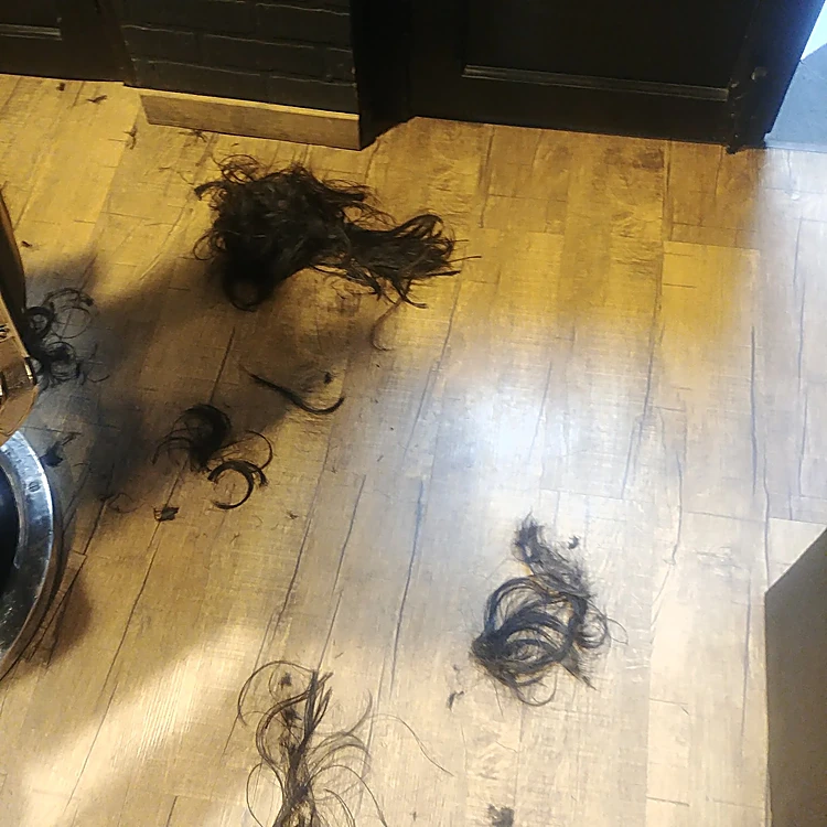 Mechones de pelo oscuro recién cortado sobre el piso de madera.