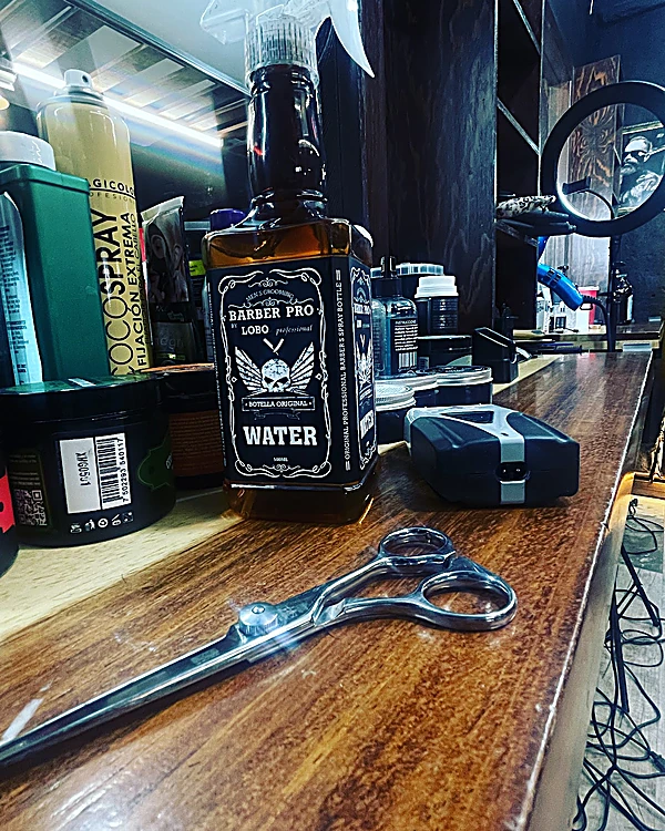 Tijera de corte y una botella de agua para barbero sobre la barra de madera.